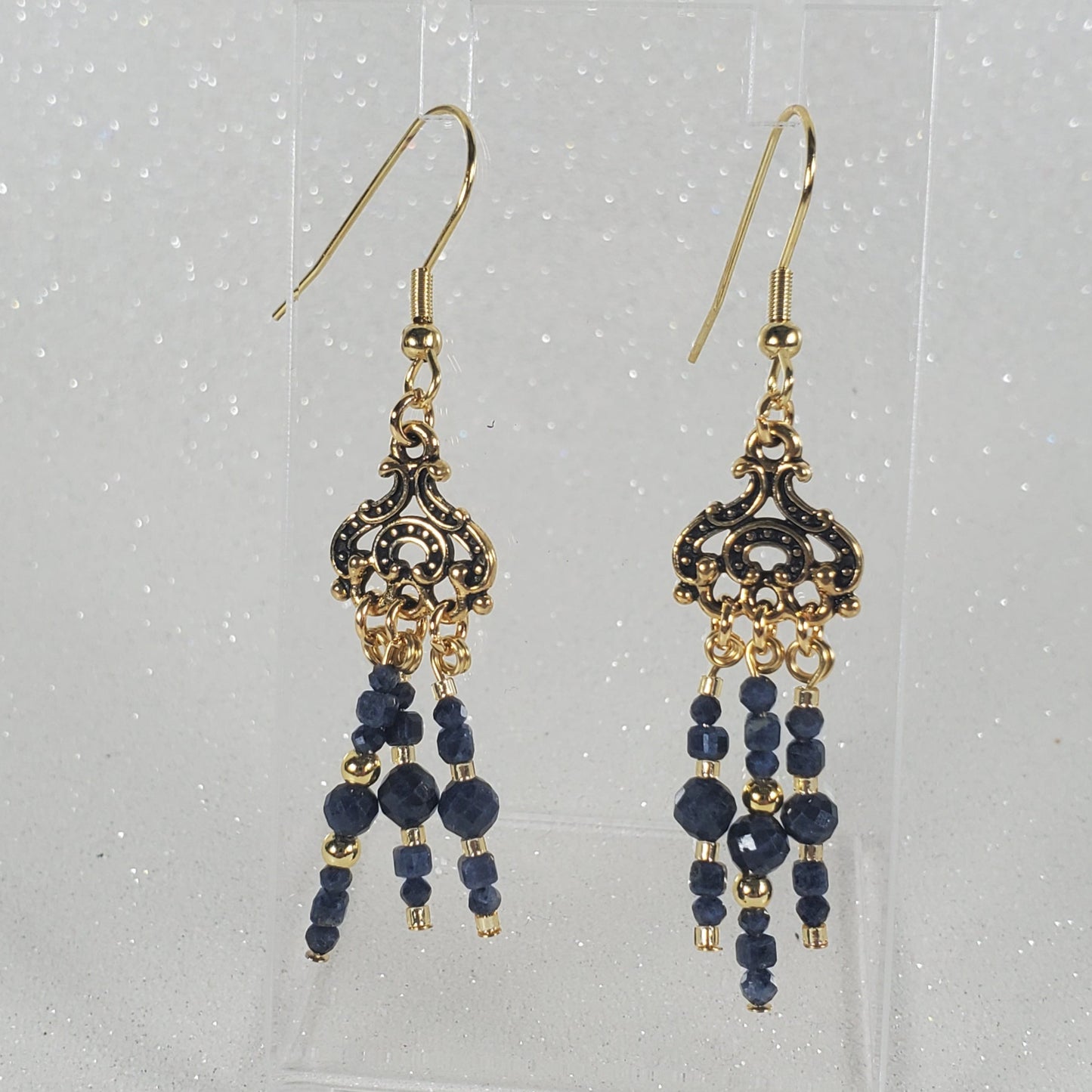 Pair of gold and blue beaded earrings on a clear card with a white background