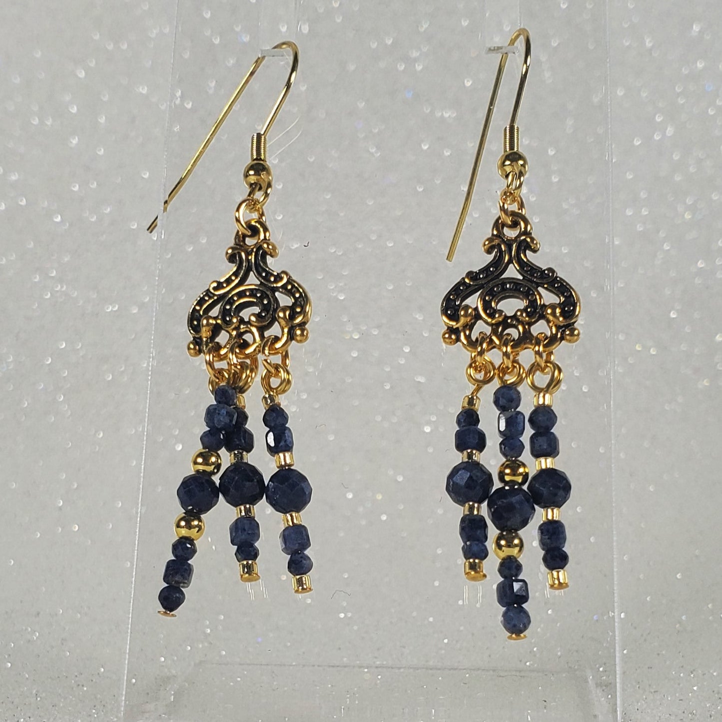Pair of gold and blue beaded earrings on a clear stand against a silver glittery background