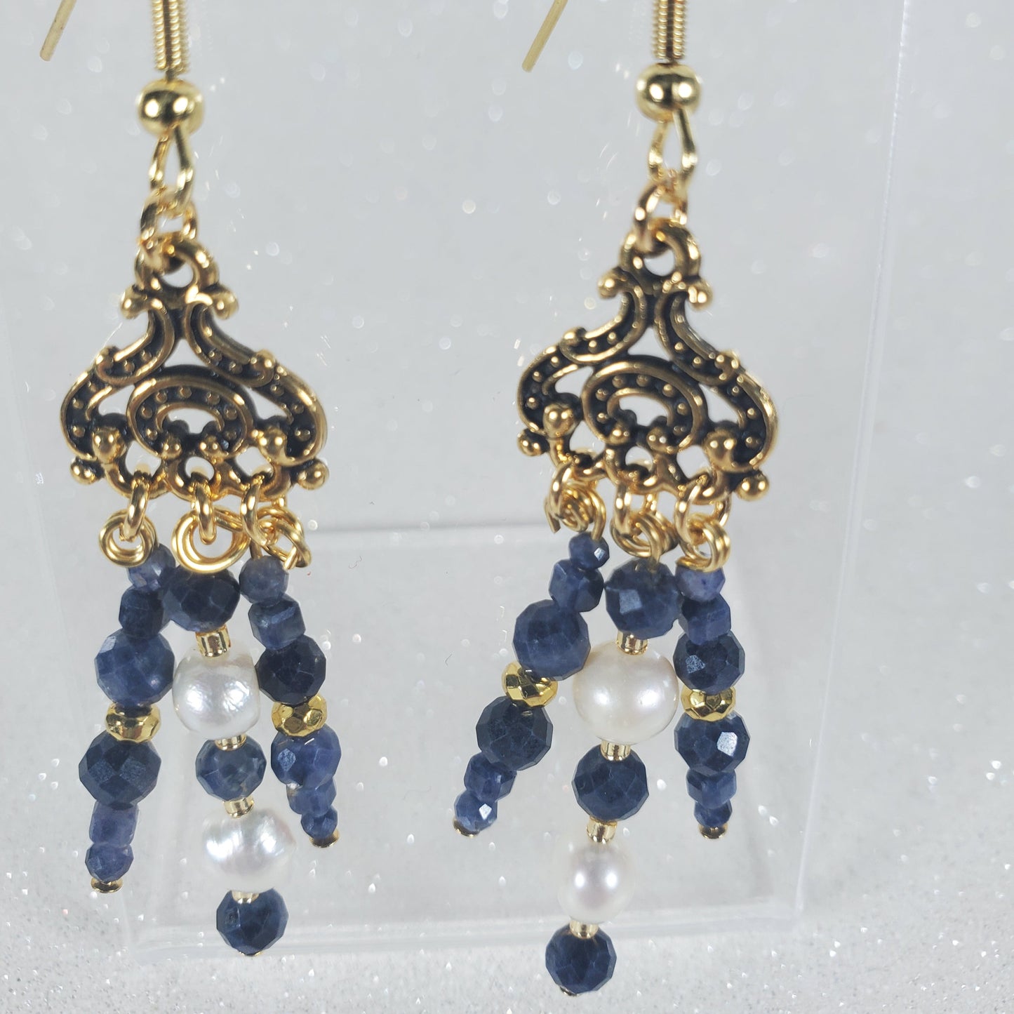Pair of gold earrings with blue and white bead accents on a light gray background