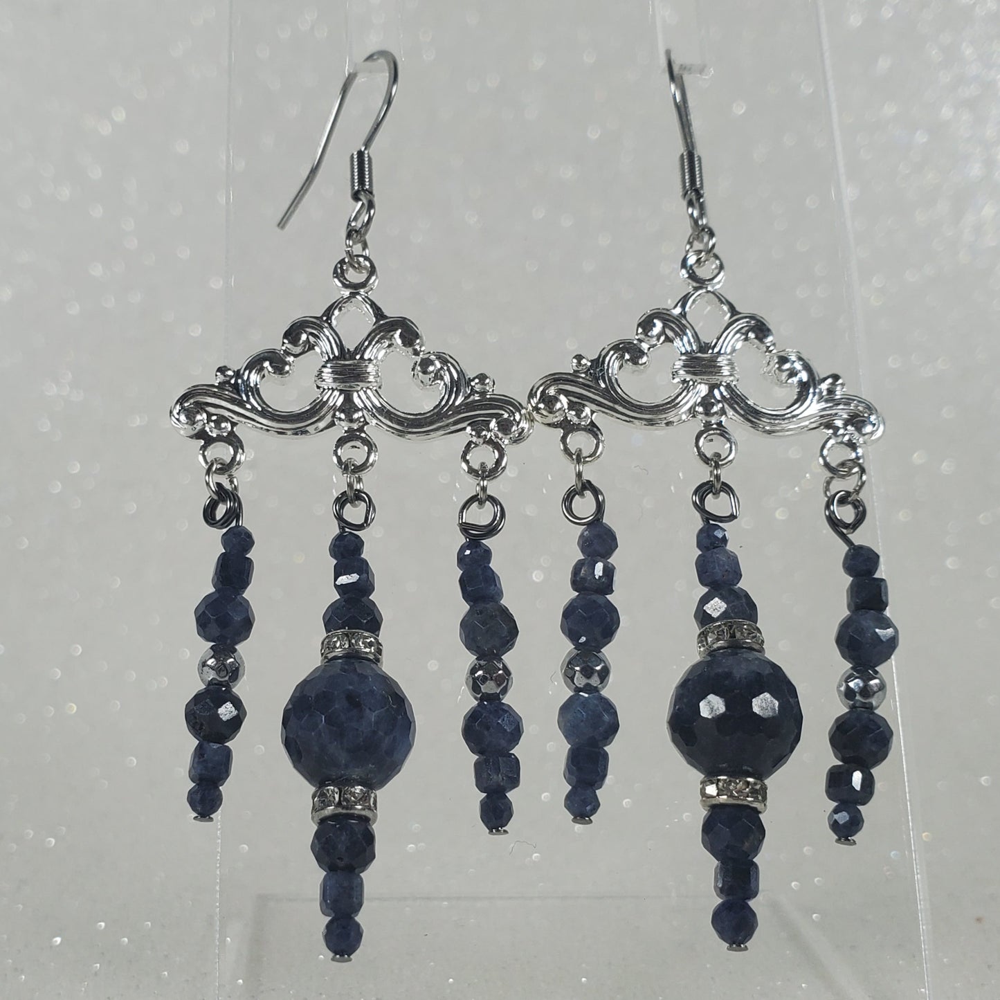 Pair of blue beaded earrings on a clear stand against a light gray background