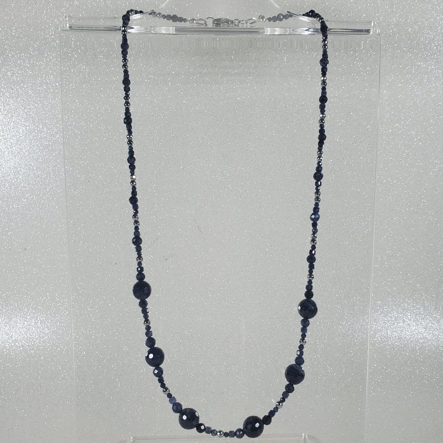 Blue beaded necklace on a clear stand against a gray background