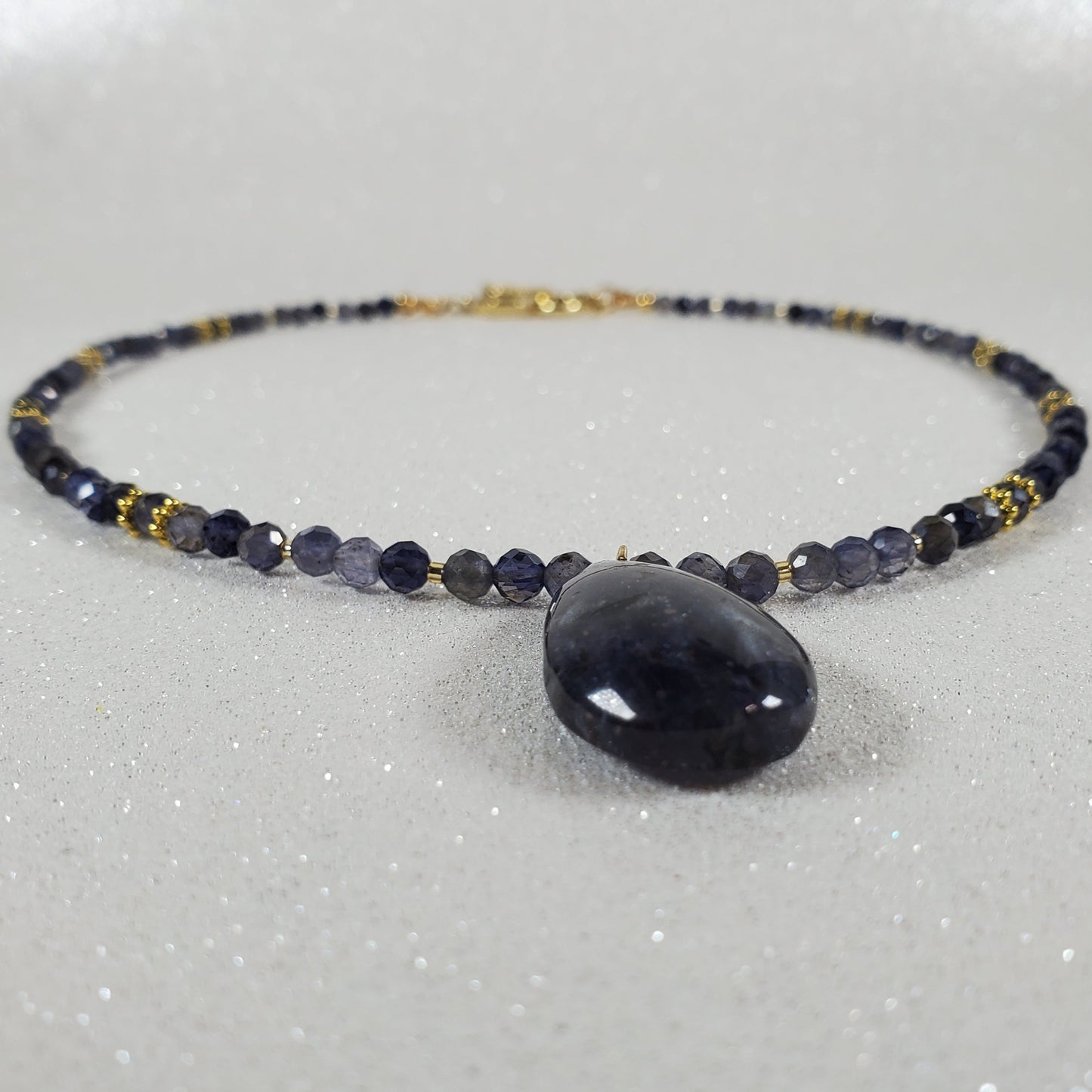Necklace with dark beads and a large central stone on a light gray background