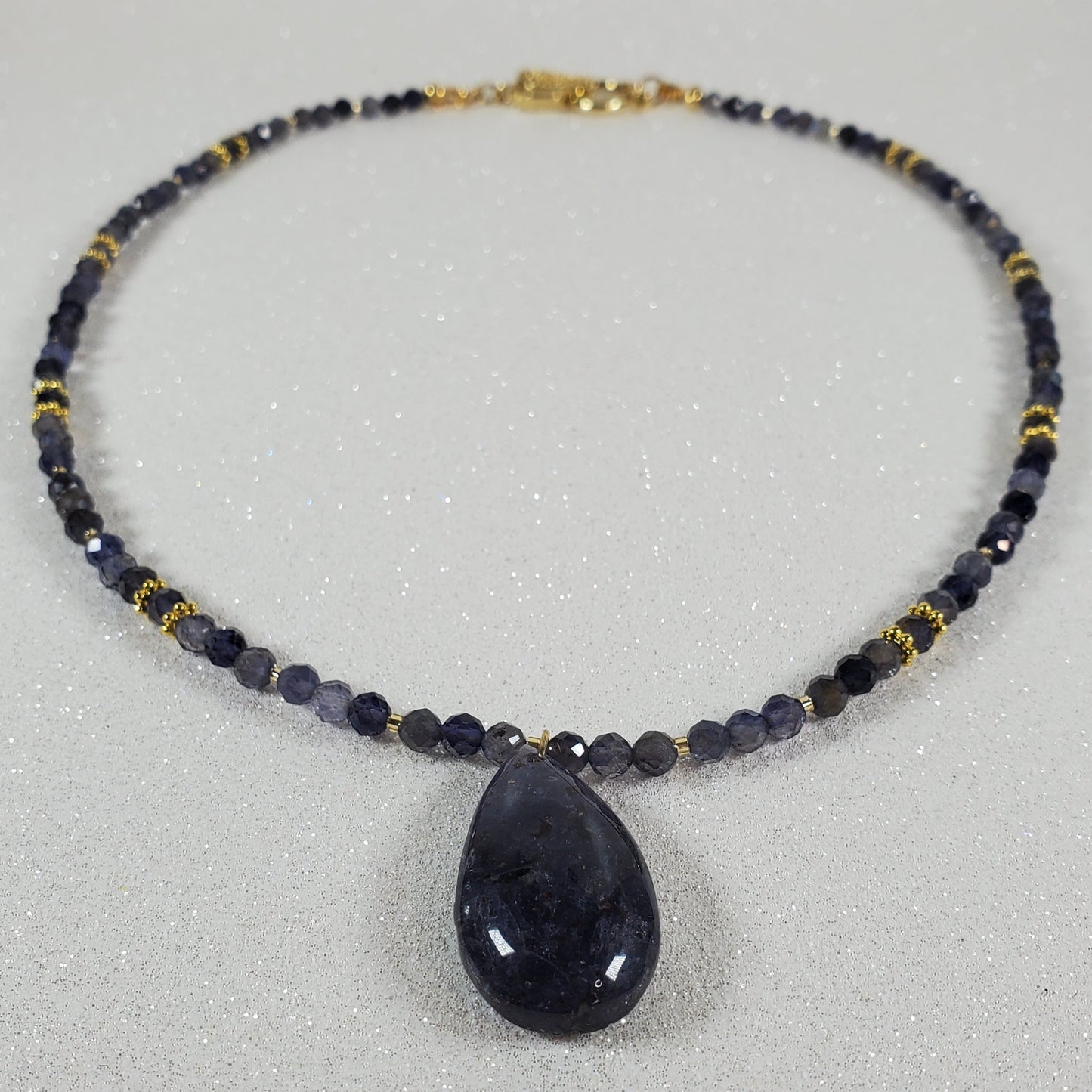 Necklace with dark beads and a large dark stone on a light gray background