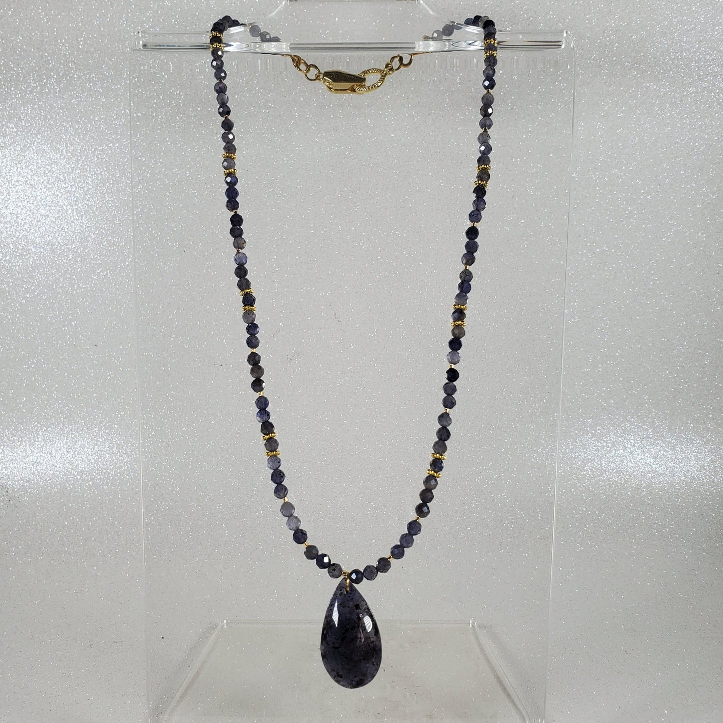 Necklace with beads and a teardrop-shaped pendant on a clear stand against a light gray background