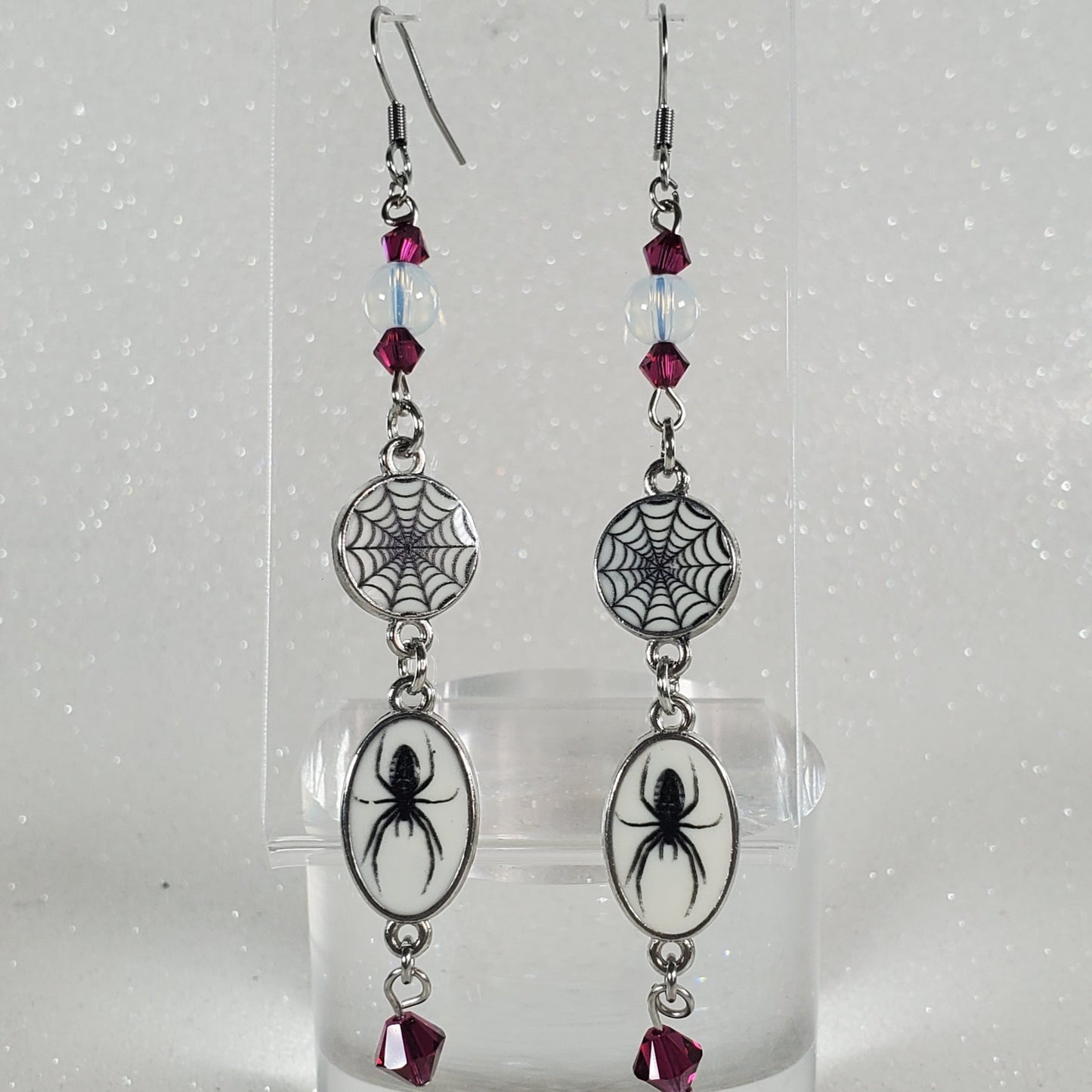 Two decorative earrings on a clear plastic stand against a white background