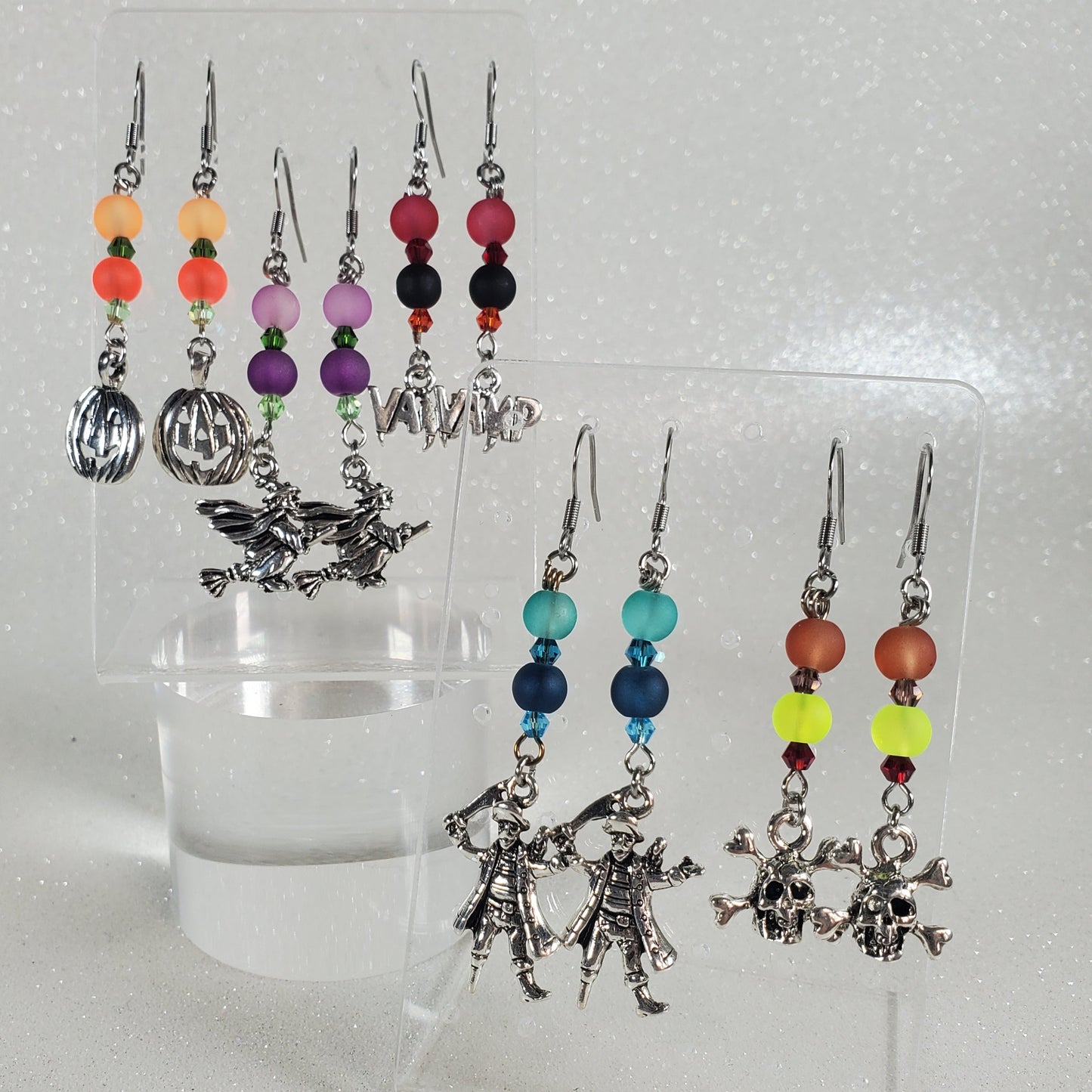 Set of earrings with colorful beads on a clear stand against a light gray background