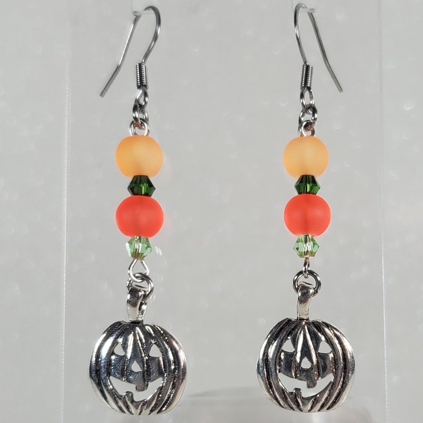 Pair of earrings with beads on a clear stand against a light gray background