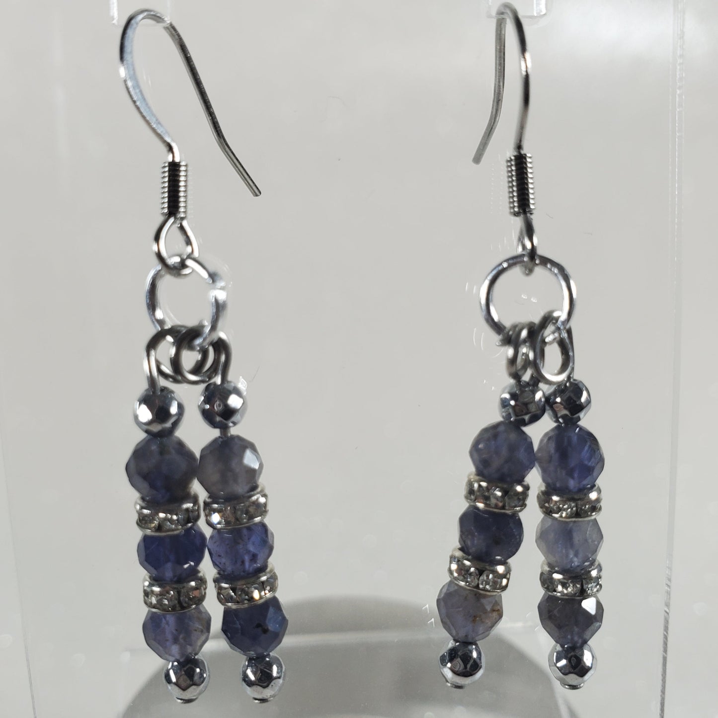 Pair of blue beaded earrings on a clear stand against a white background