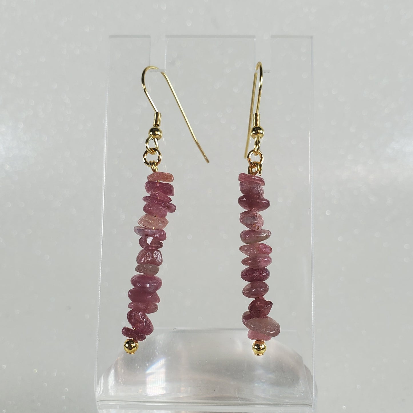 Pair of earrings with pink gemstones on a clear stand against a white background