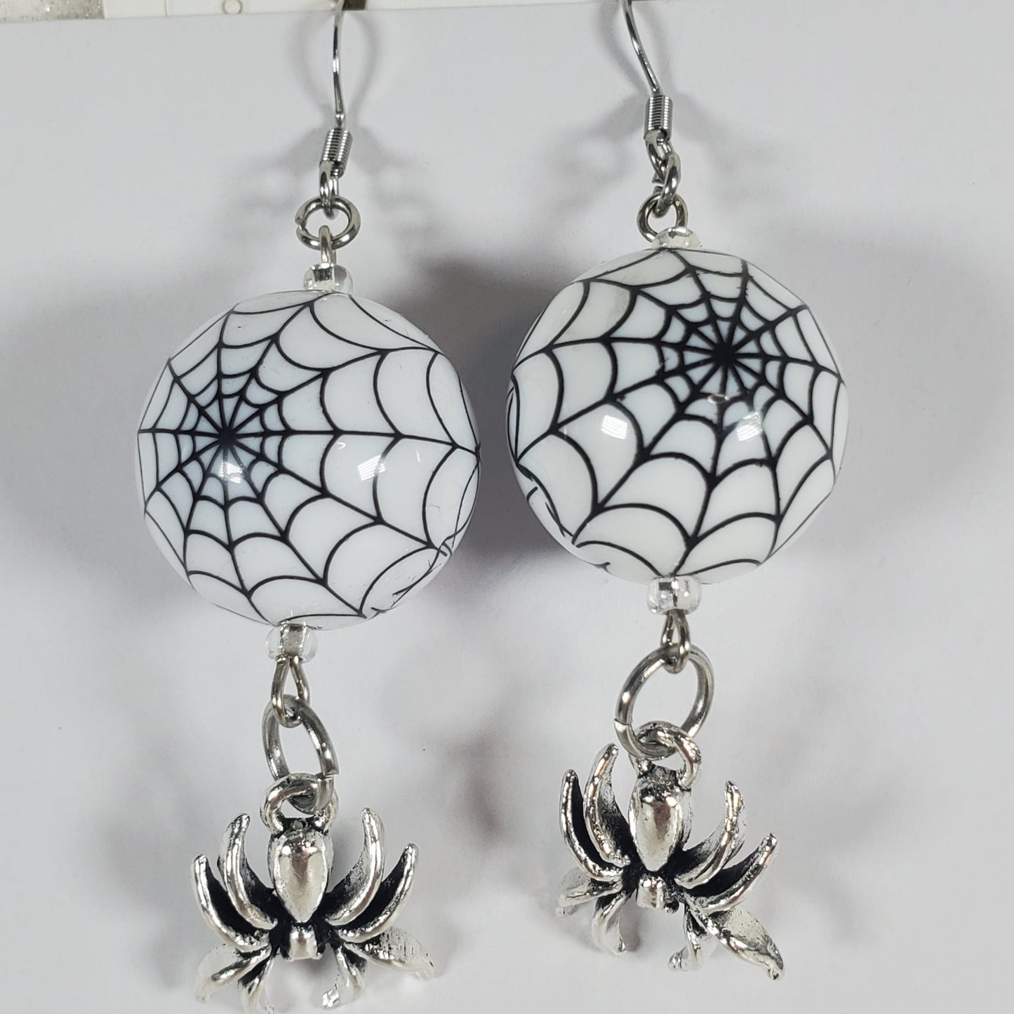 Spider web and spider earrings on a white card with a gray background