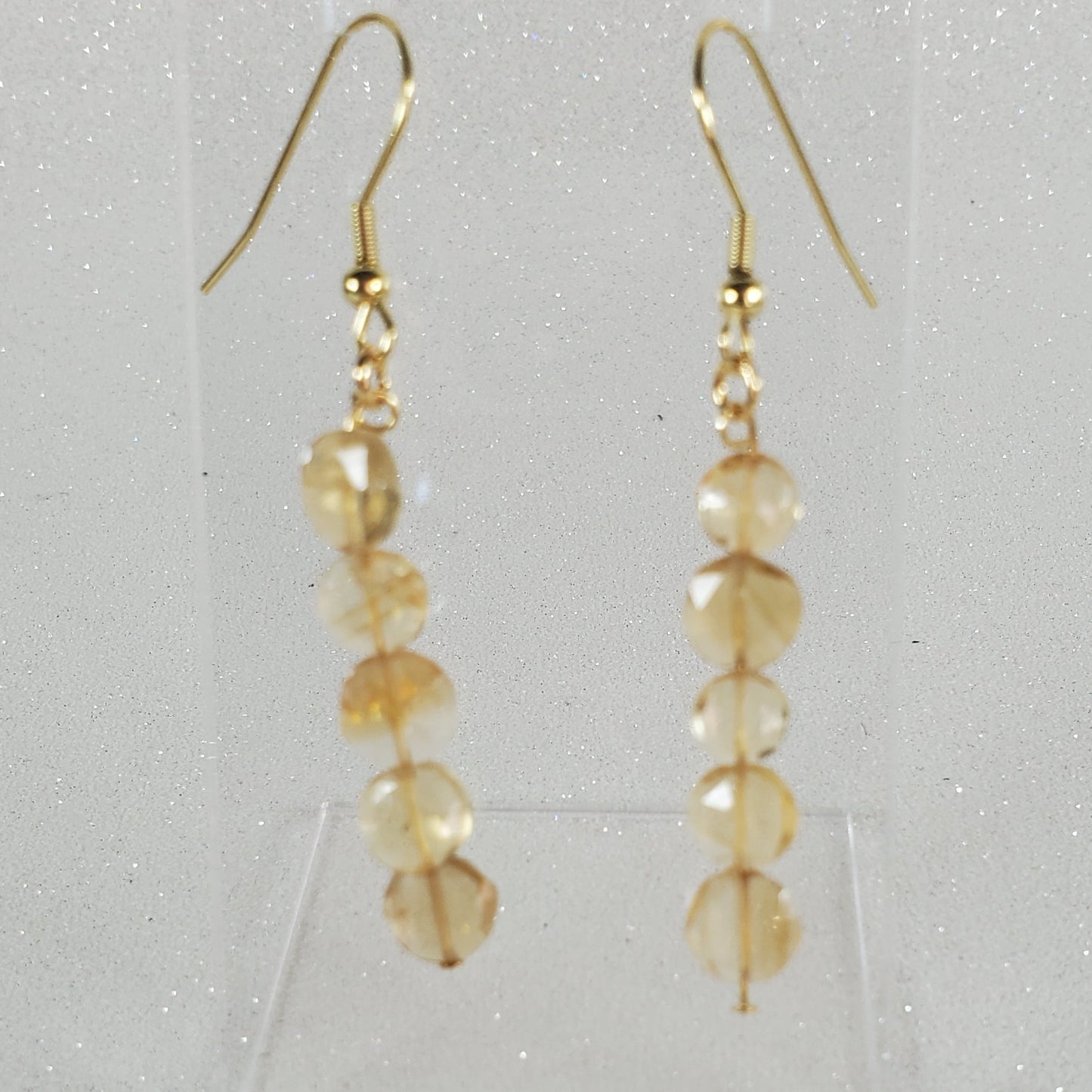 Gold beaded earrings on a clear stand against a light gray background