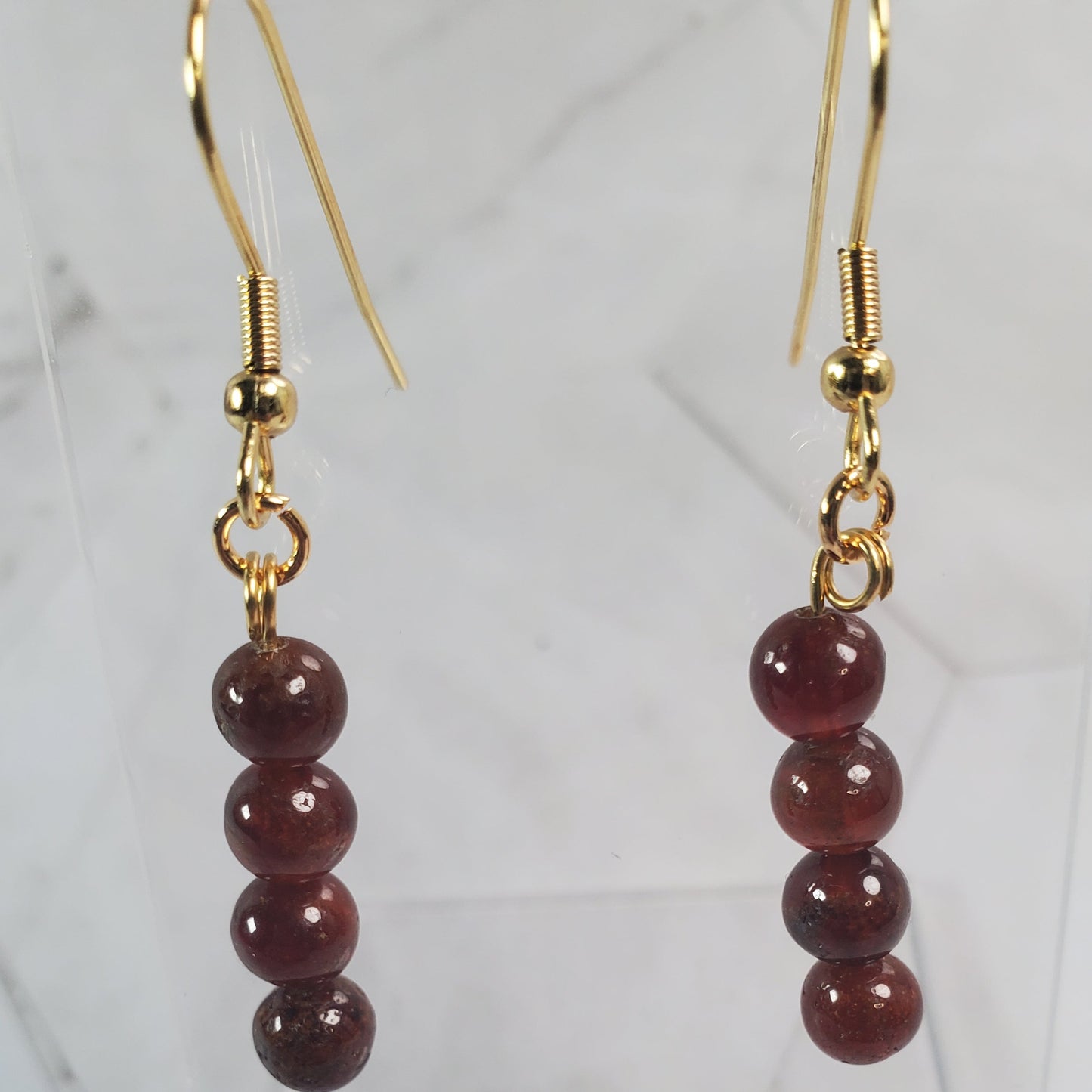 Gold earrings with red beads on a marble surface