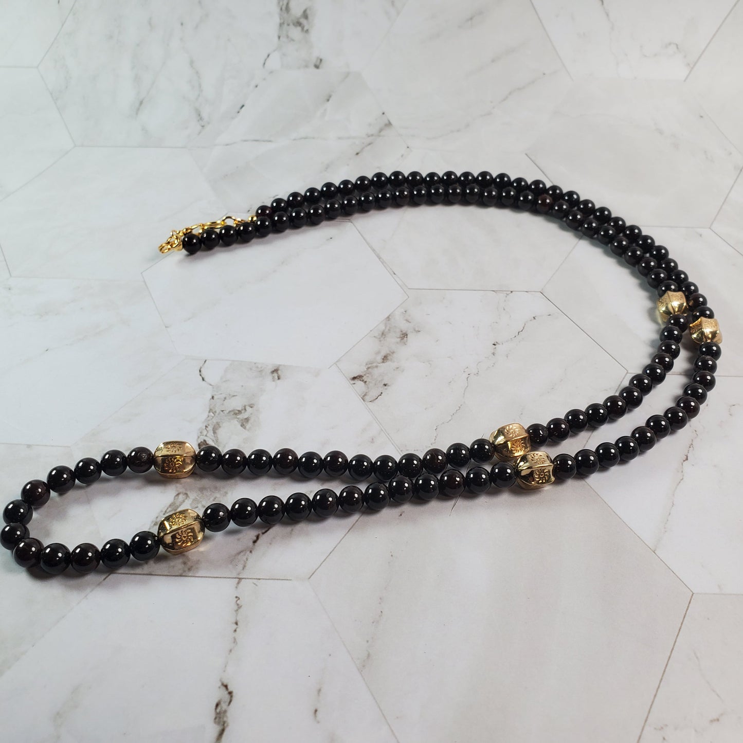 Deep red beaded necklace with gold accents on a marble surface