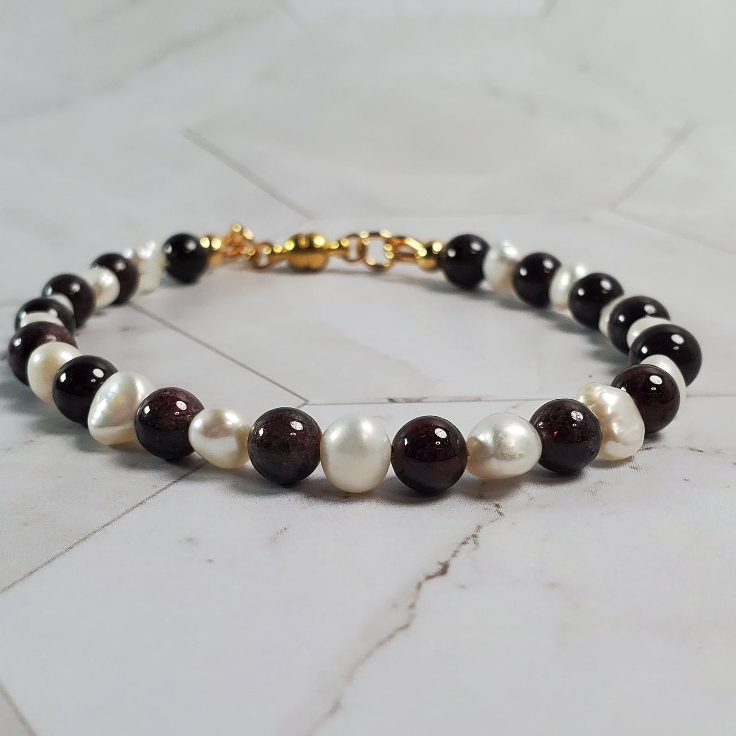 Beaded bracelet with red, white, and gold beads on a marble surface