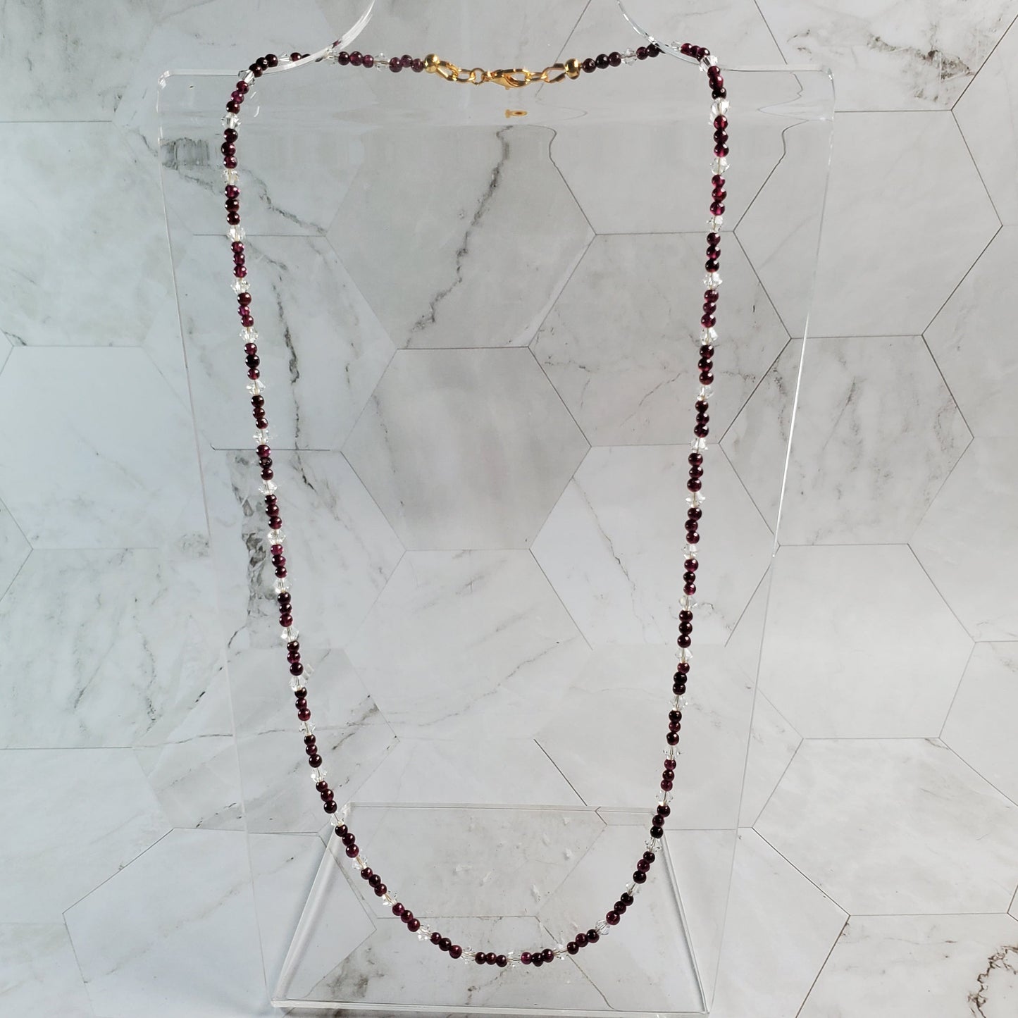 Garnet and crystal gemstone necklace on a marble tile background
