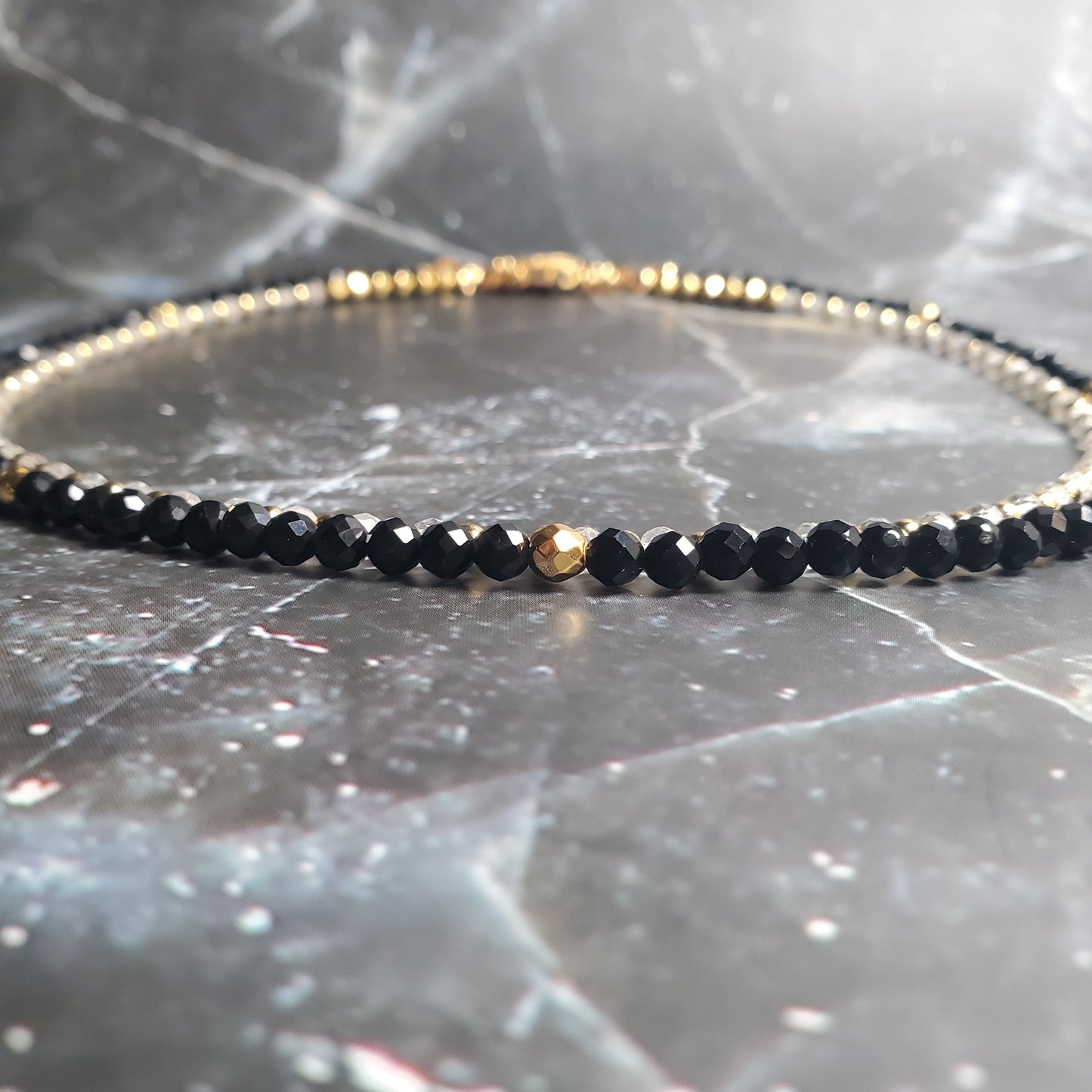 Black beaded Necklace with gold accents on a gray marble surface