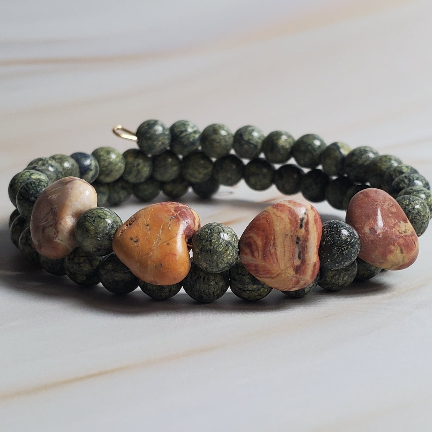 Beaded bracelet with green, brown, and beige beads on a light marble background