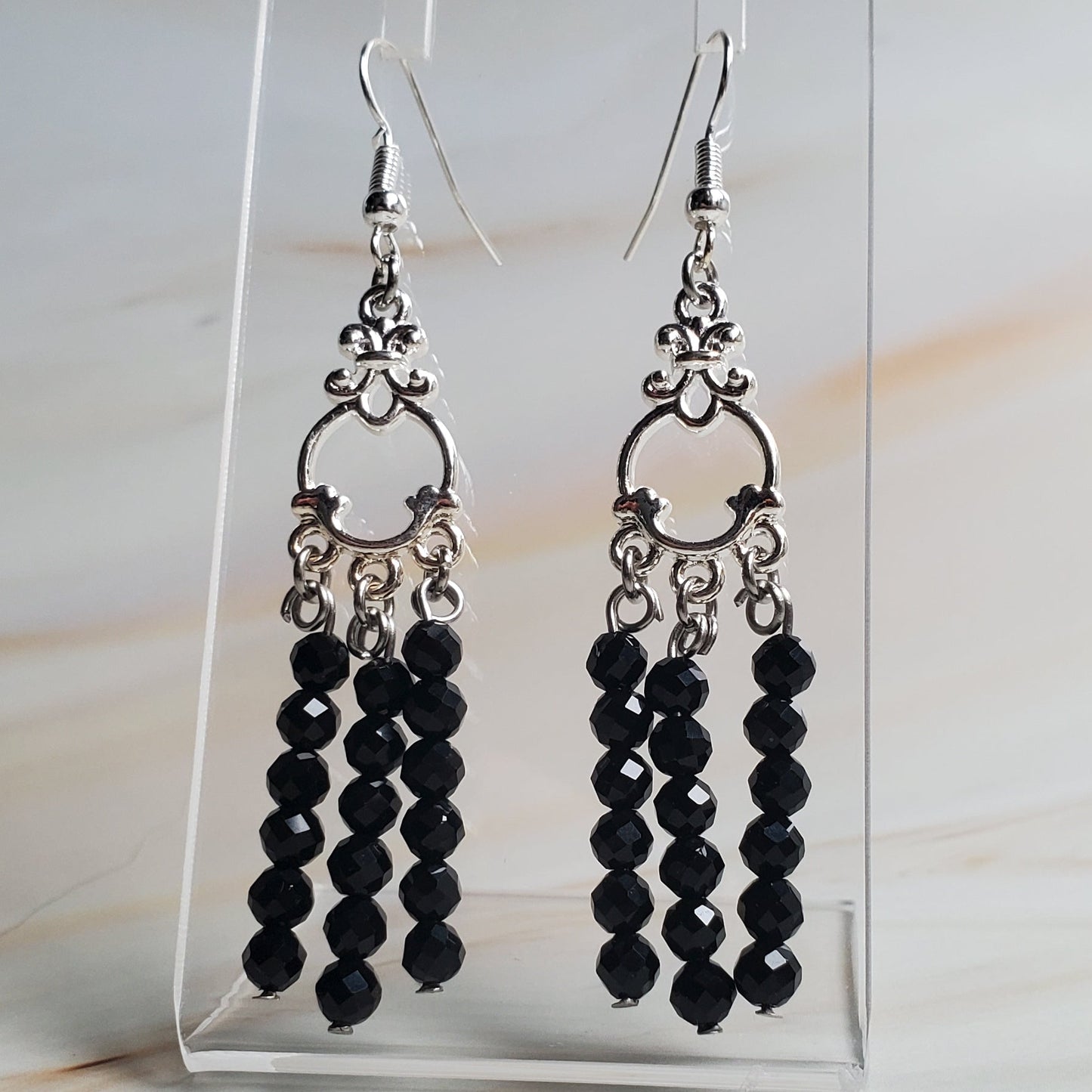 Black beaded earrings on a clear display card against a marble background