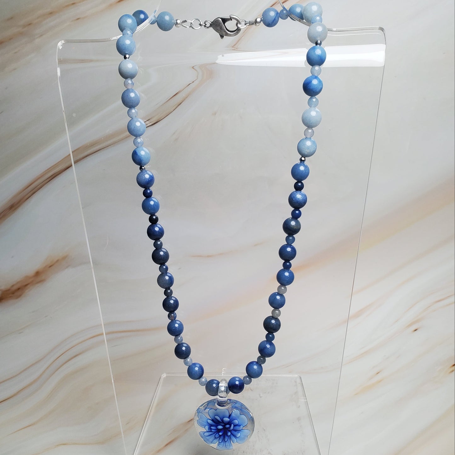 Blue beaded necklace on a clear stand against a marble background