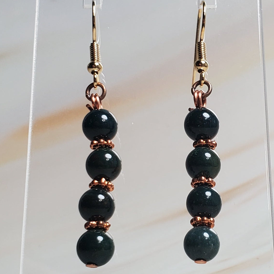 Green beaded earrings on a clear stand against a marble background