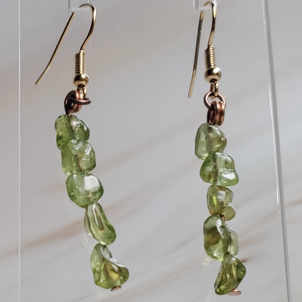 Green beaded earrings on a clear stand against a marble background