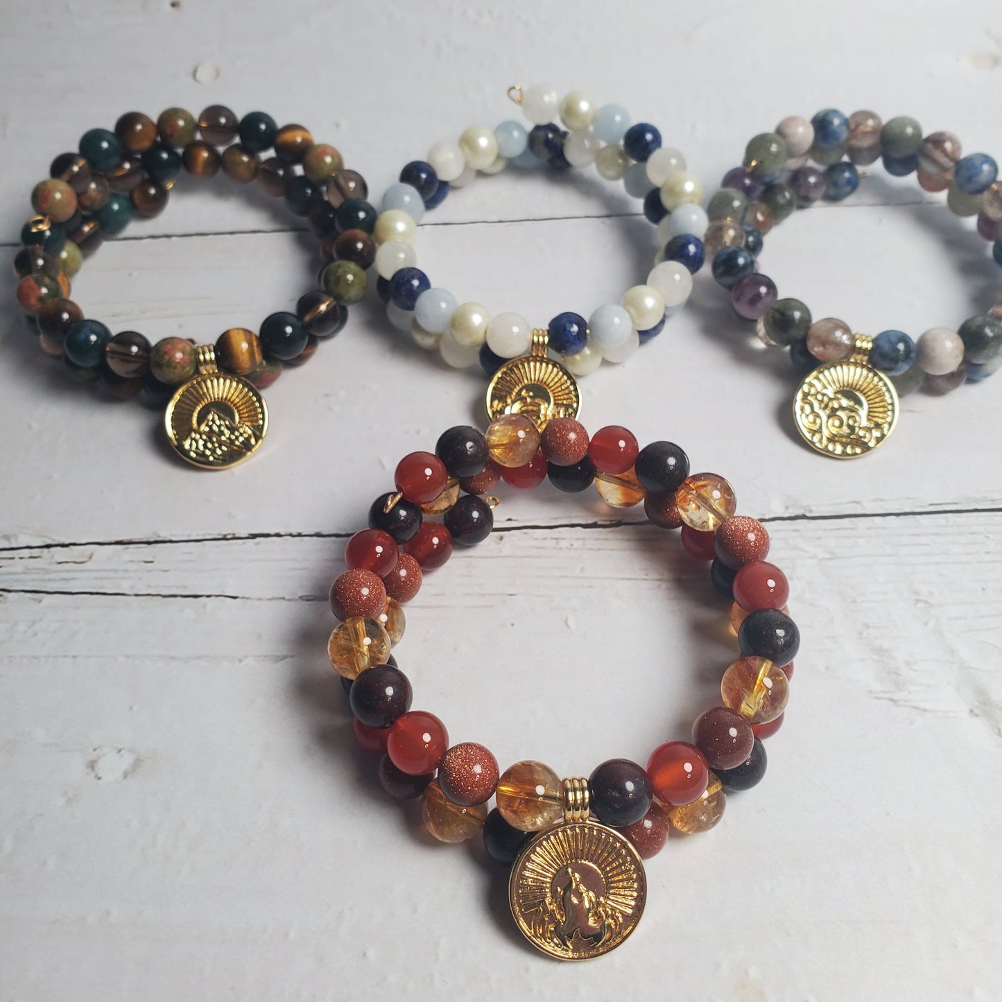 Three beaded bracelets with gold coins on a white wooden surface