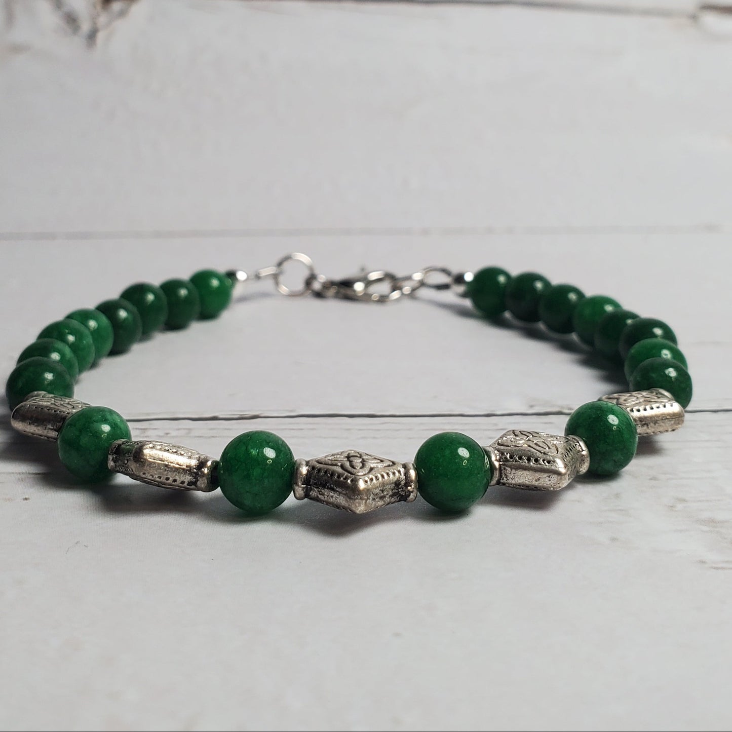 Green beaded bracelet with silver accents on a light wooden surface