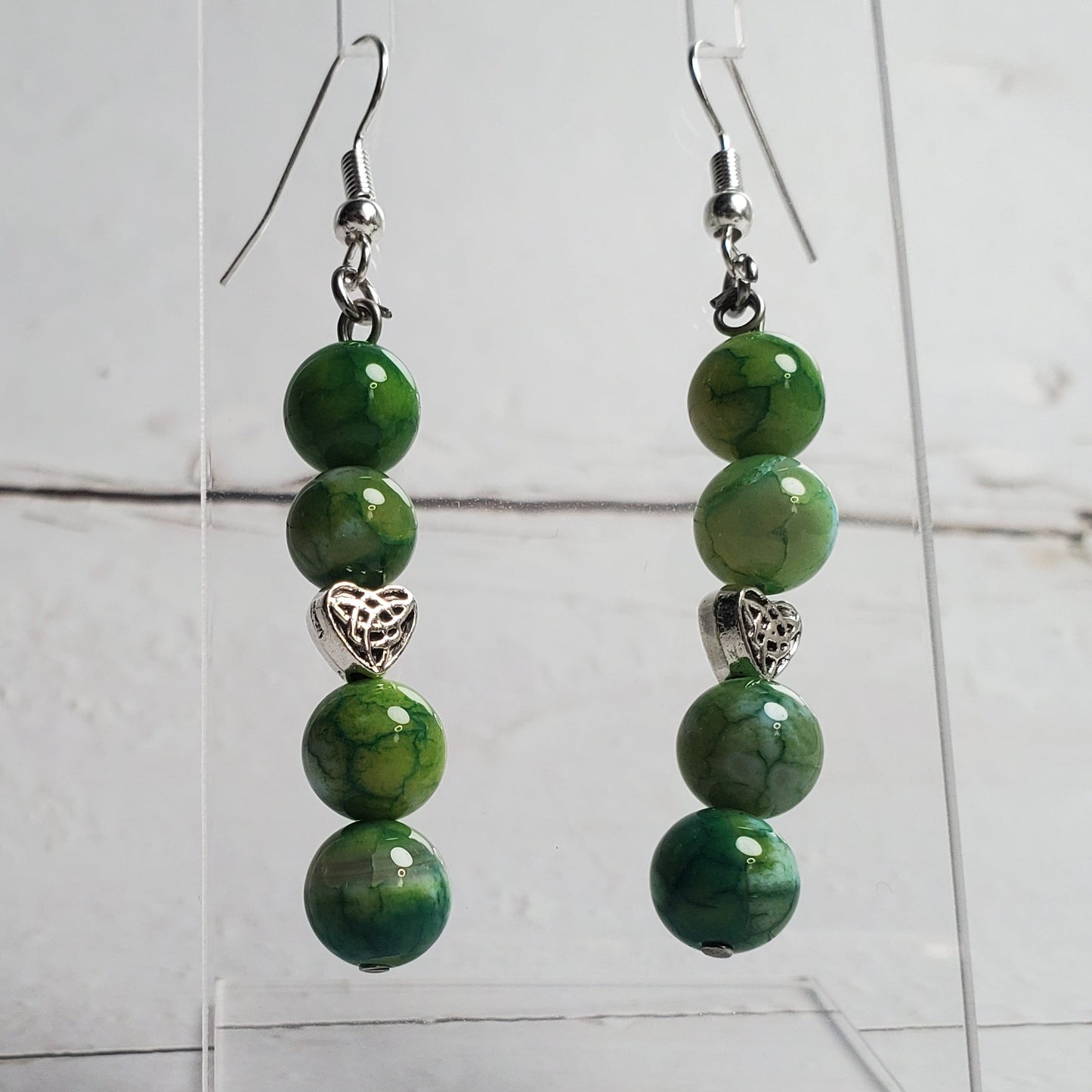Green beaded earrings on a clear stand against a white wooden background