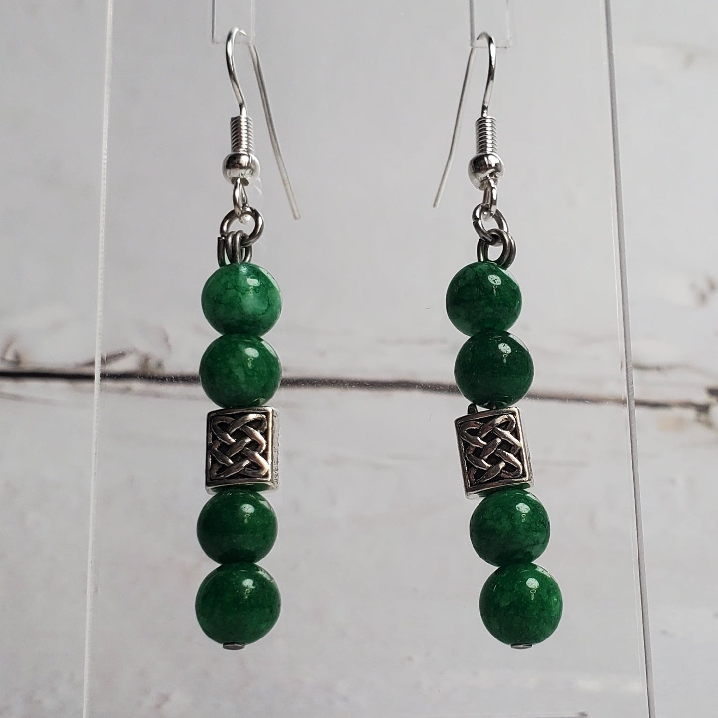 Green beaded earrings on a clear stand against a white wooden background