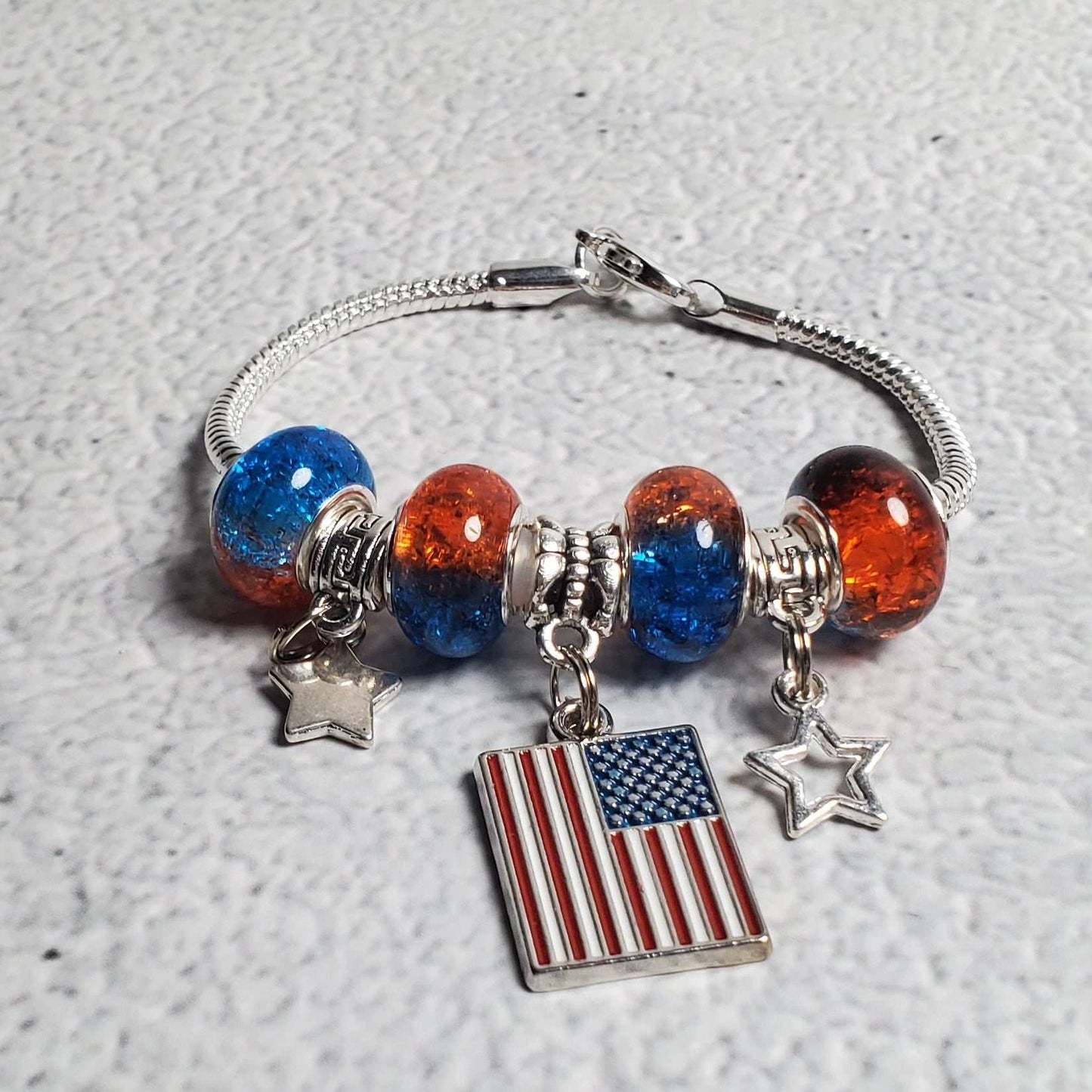 Child's 4th of July charm bracelet with red and blue beads, pewter stars, and American flag centerpiece on a snake-chain