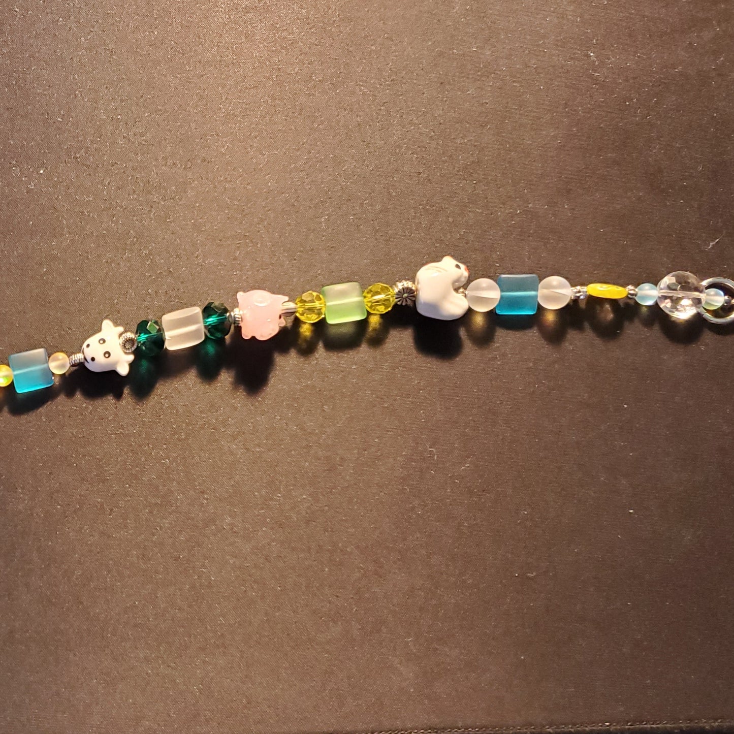 A handmade beaded suncatcher featuring colorful translucent and opaque beads, small animal charms, and a clear teardrop crystal at the bottom.