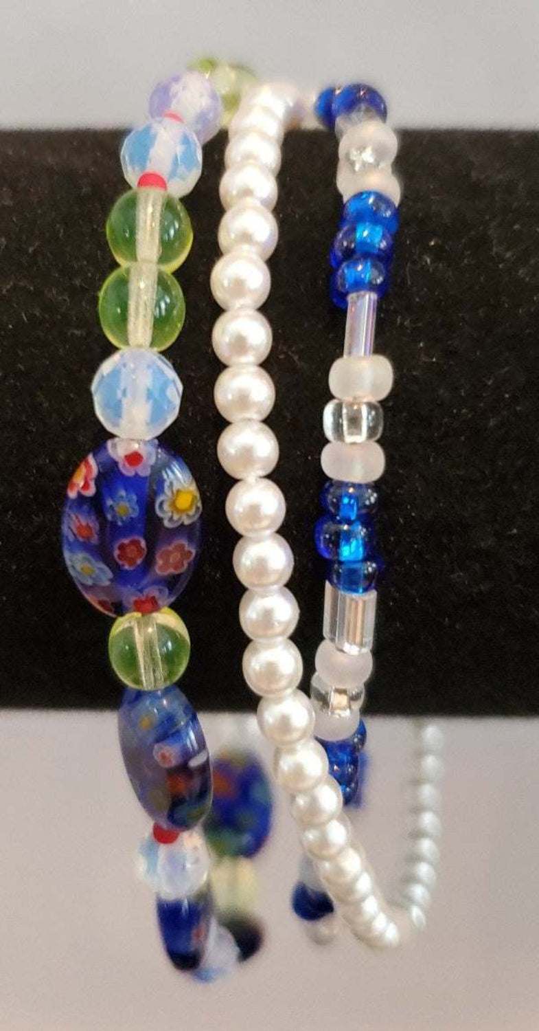 Blue multistrand millefiori bracelet with floral beads, crystals, and white pearls on black background