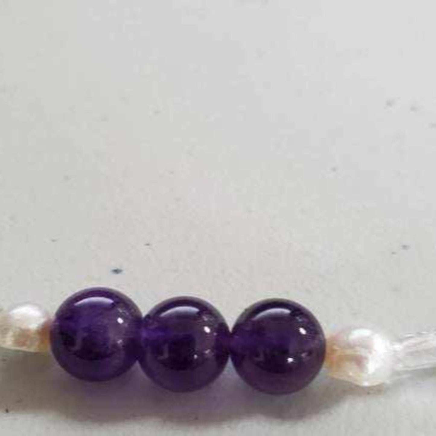 Close-up of a gemstone necklace featuring three polished amethyst beads and two freshwater pearls on a light background