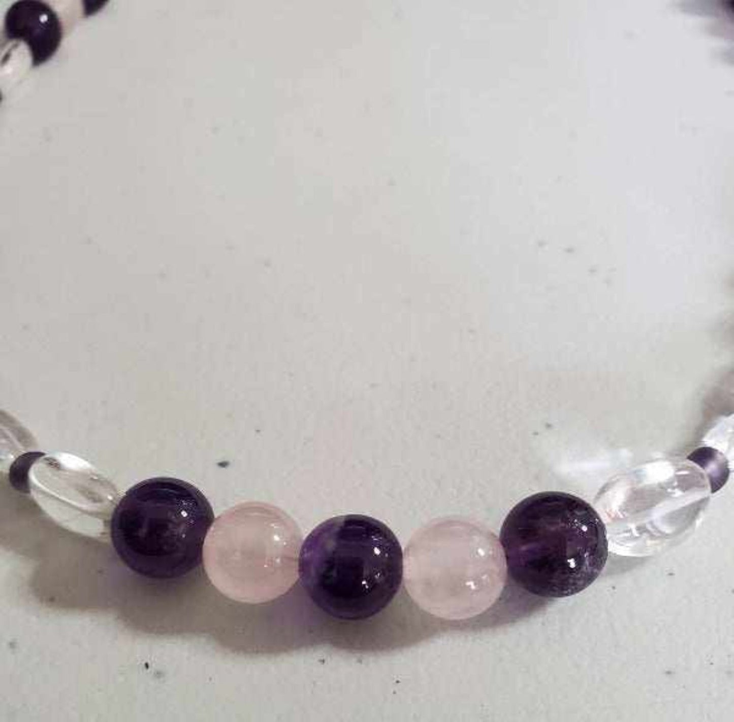 Close-up of a gemstone necklace featuring alternating amethyst and rose quartz beads with clear glass accents.