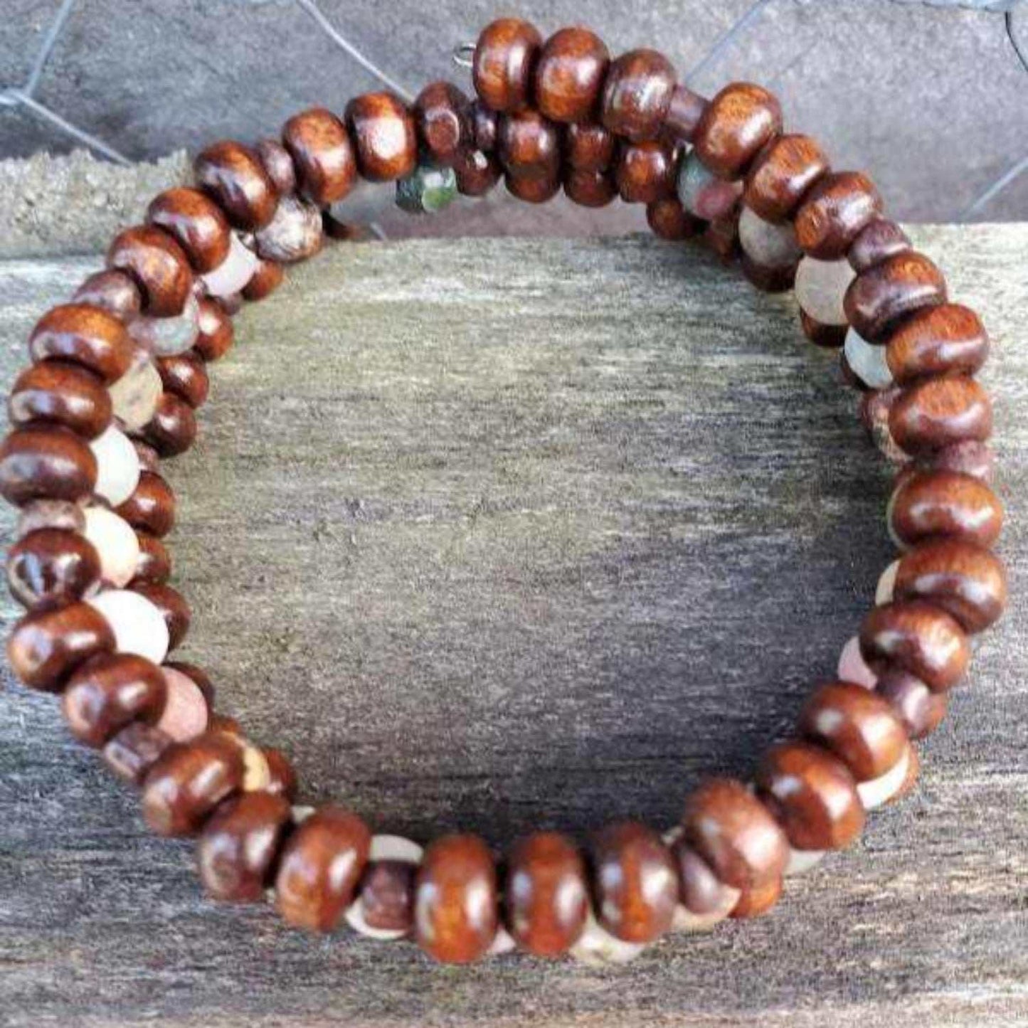 Earth-tone gemstone cuff bracelet with wooden beads and natural stone accents on a rustic wooden surface