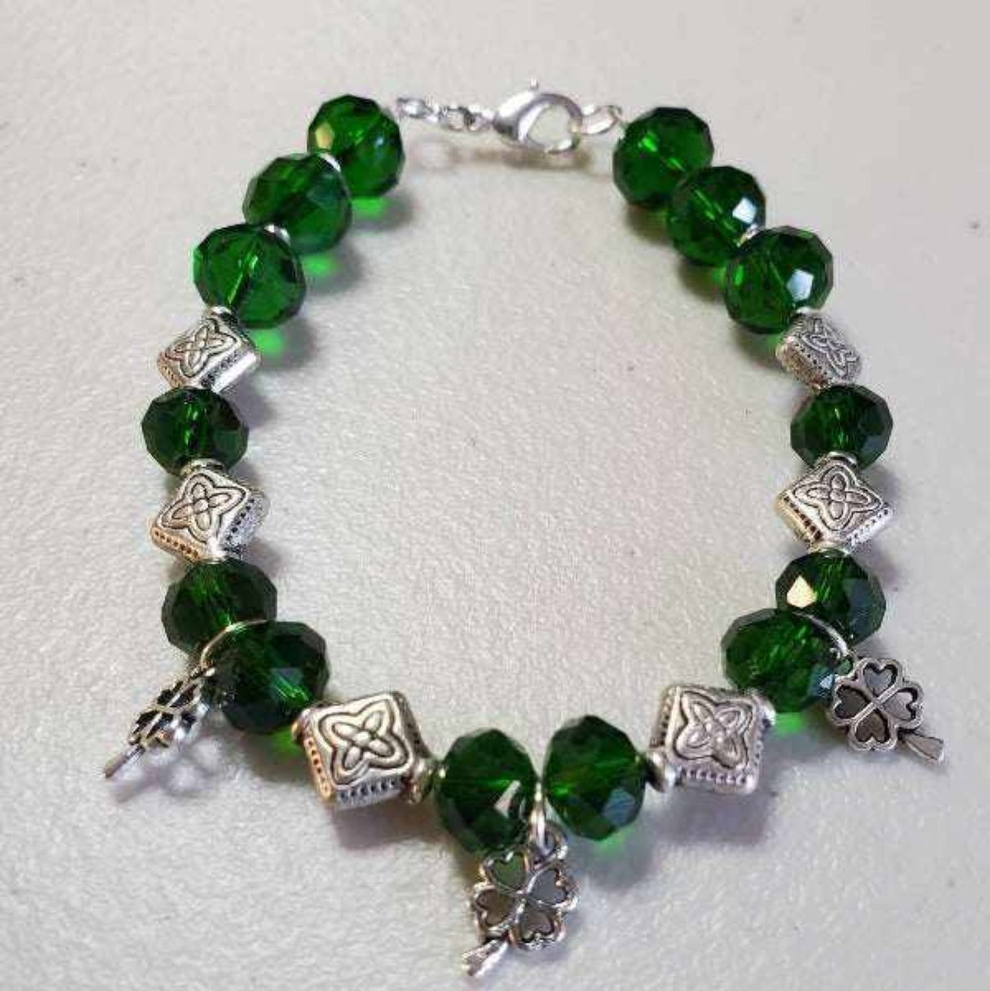 Green beaded shamrock bracelet with Celtic knot spacers and charms on white background
