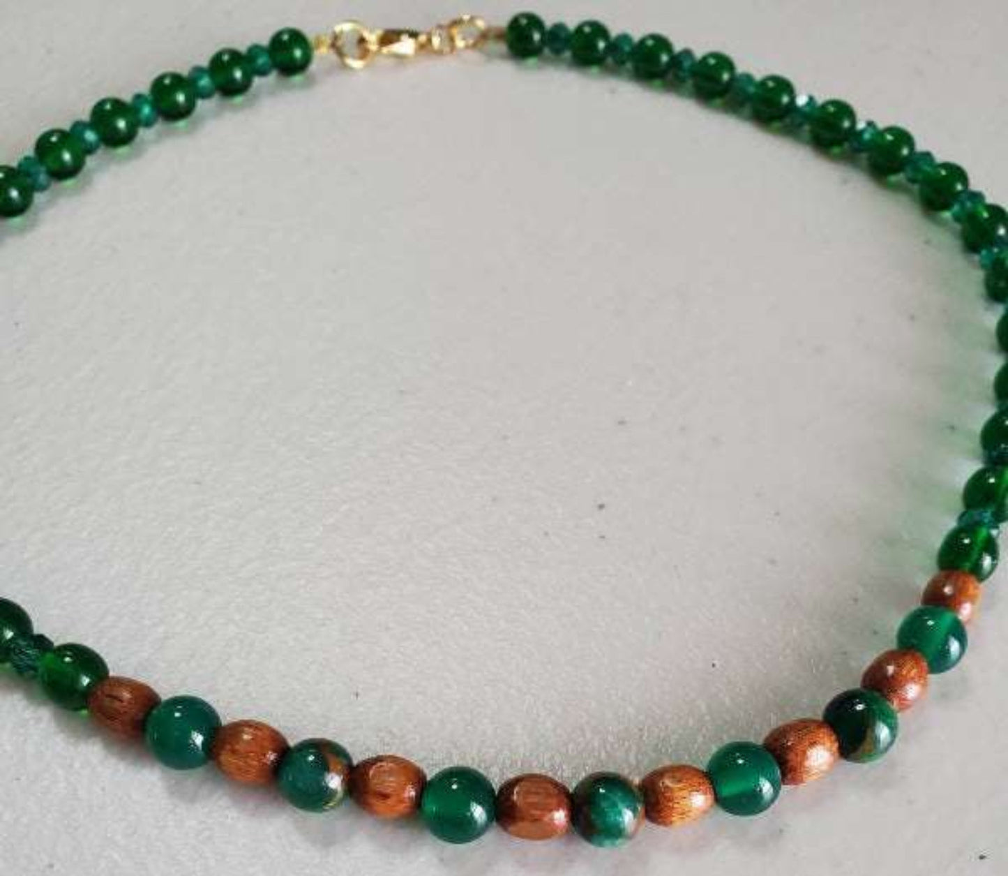 Emerald choker necklace with green and brown beads and gold clasp on light background