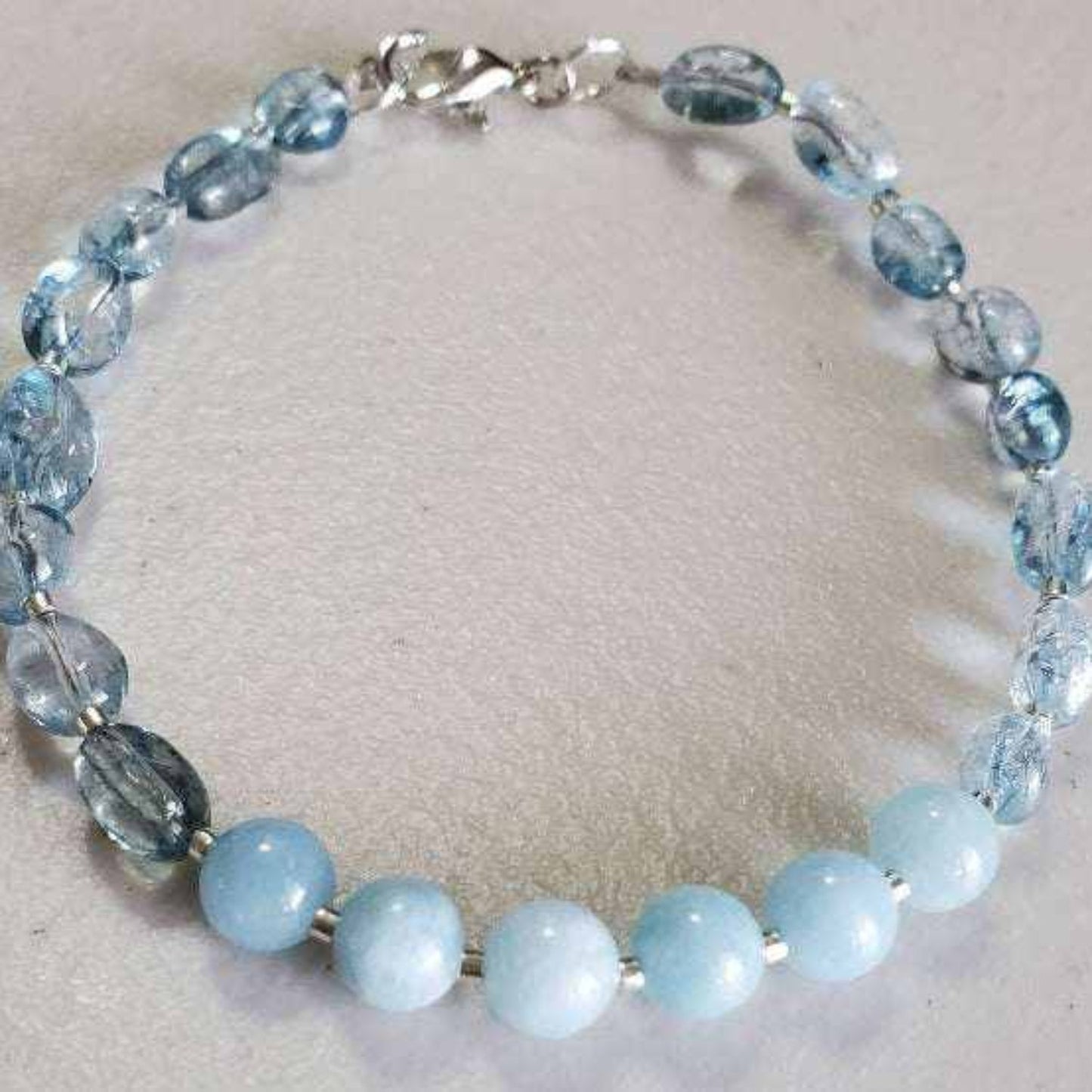 Aquamarine gemstone bracelet with polished blue beads and silver lobster clasp on gray background