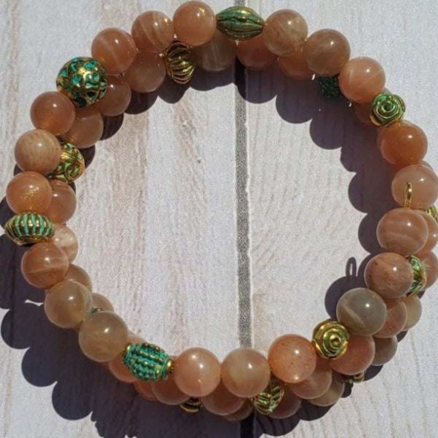 Peach Moonstone cuff bracelet with gold and turquoise brass accents on light wooden background