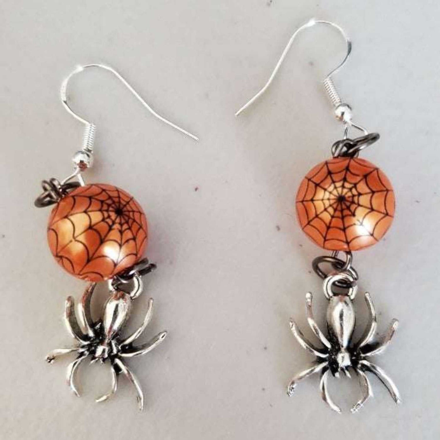Pair of dangle spiderweb earrings with orange acrylic webs and silver pewter spider charms