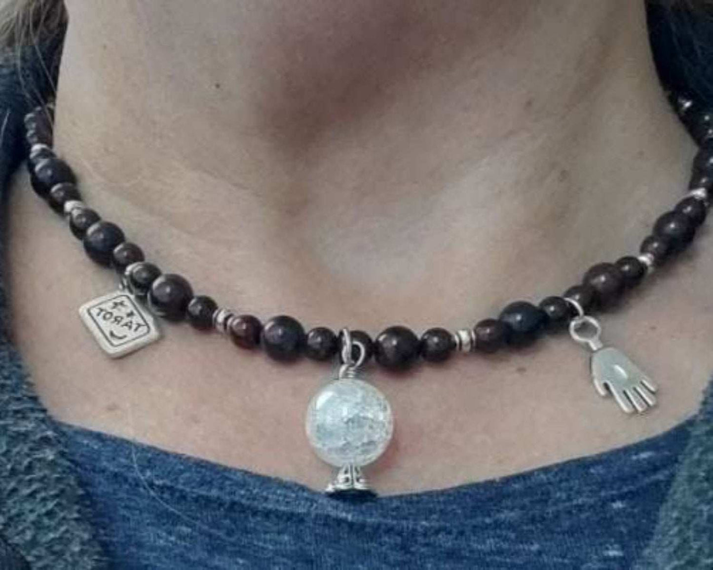 Close-up of a mystical gemstone necklace with pewter tarot, crystal ball, and palmistry hand charms on dark beads