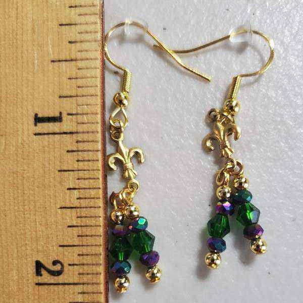 Drop style Mardi Gras earrings with green and purple crystals and gold fleur-de-lis charm next to ruler for size reference