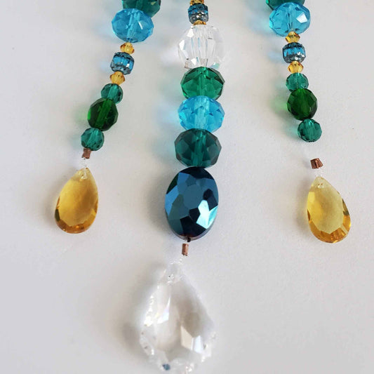 Handcrafted crystal suncatcher with antiqued brass peacock and blue, green, and yellow glass beads.