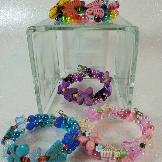 Colorful child's butterfly bracelets with beads and butterfly charms on flexible memory wire displayed on and around a clear glass block