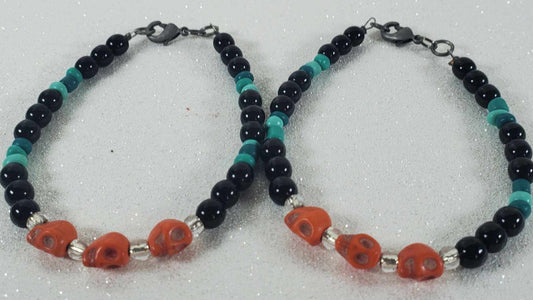Pair of Skull Bracelets with orange Howlite skull beads, black and turquoise round beads, and silver accents with lobster claw clasps on a glittery surface.