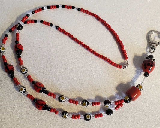 Red and black ladybug lanyard with glass beads and floral accents, featuring a magnetic clasp.