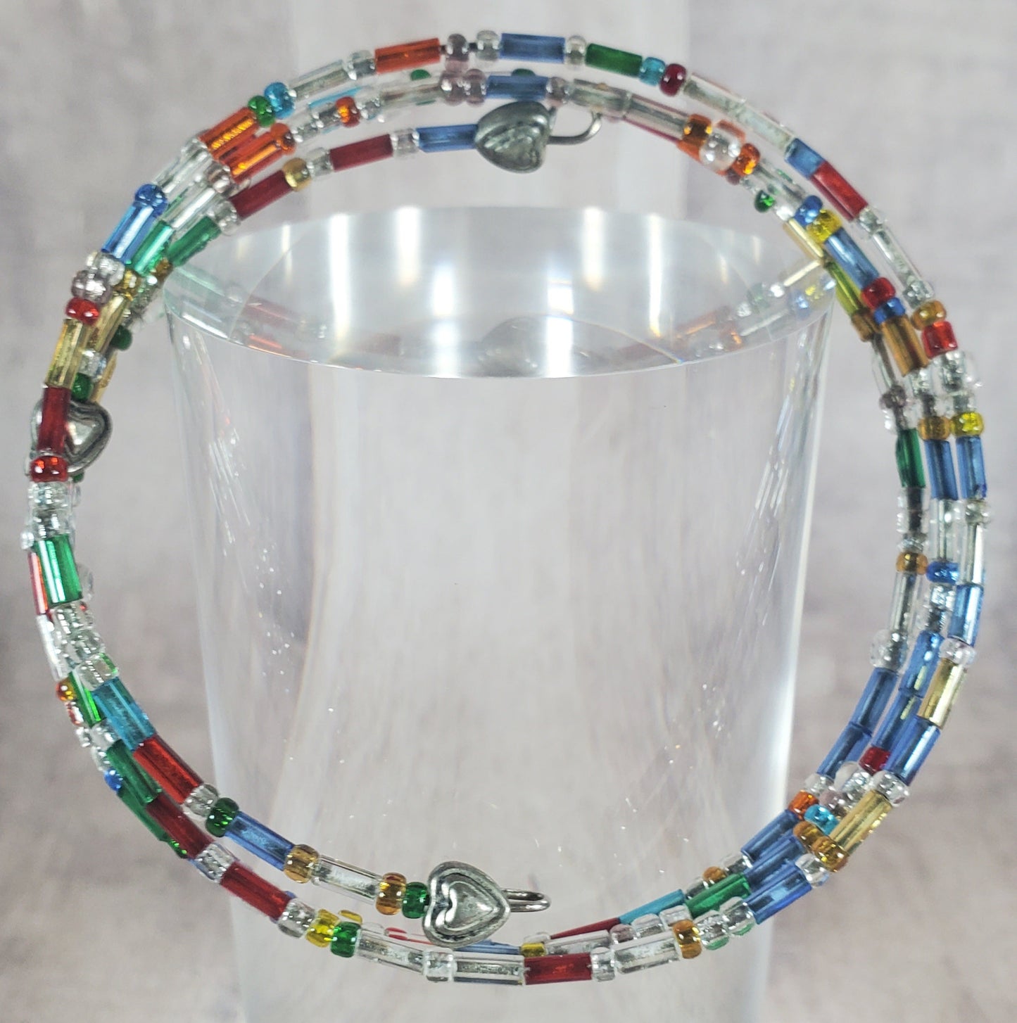 Colorful beaded necklace on a clear stand against a light background