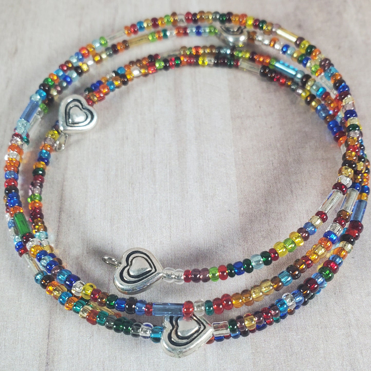 Colorful beaded necklace with silver heart pendants on a light gray background