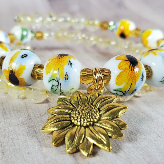Floral bracelet featuring porcelain sunflower beads, citrine accents, and a brass sunflower charm on adjustable memory wire