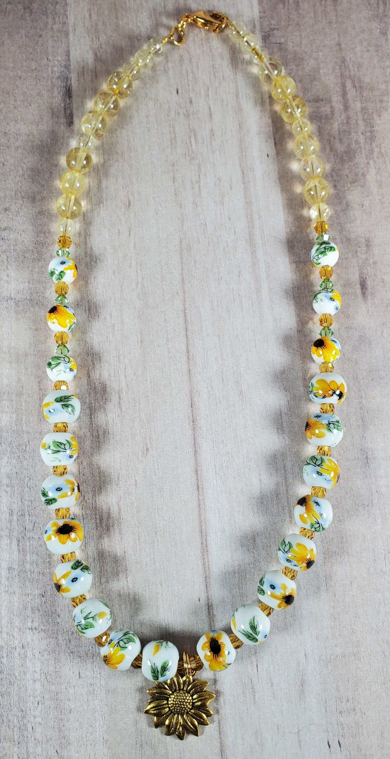 Floral necklace with porcelain sunflower beads, citrine gemstones, and brass sunflower charm on a 16-inch strand.
